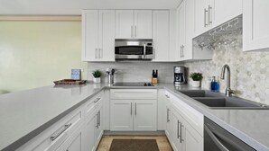 Una cocina moderna con armarios blancos, un microondas de acero inoxidable y un lavamanos.