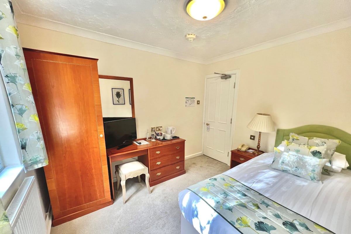 Une chambre d’hôtel comprenant un lit, un bureau avec une chaise, une télévision, une porte et une petite table avec une lampe.