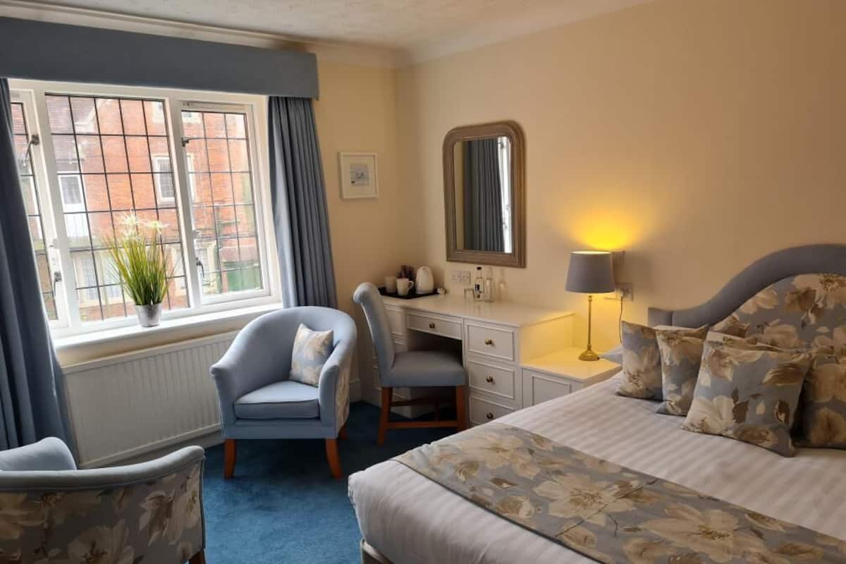 Une chambre d’hôtel avec un lit, un bureau, une chaise, une fenêtre avec des rideaux et une lampe.