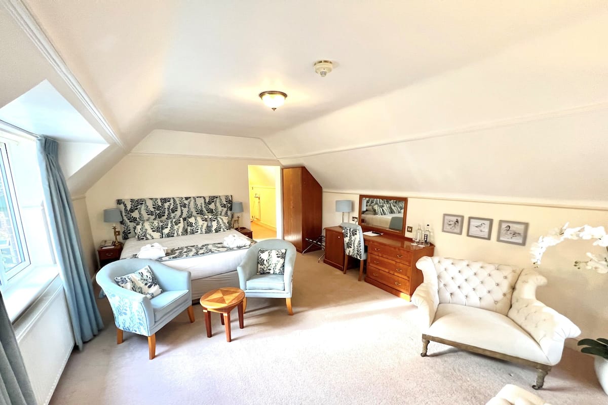 Une chambre à coucher comprenant un lit, deux fauteuils, une commode et une coiffeuse avec un miroir.