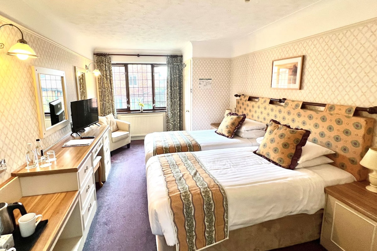 Une chambre d’hôtel avec deux lits, un bureau avec une télévision et une fenêtre avec des rideaux.