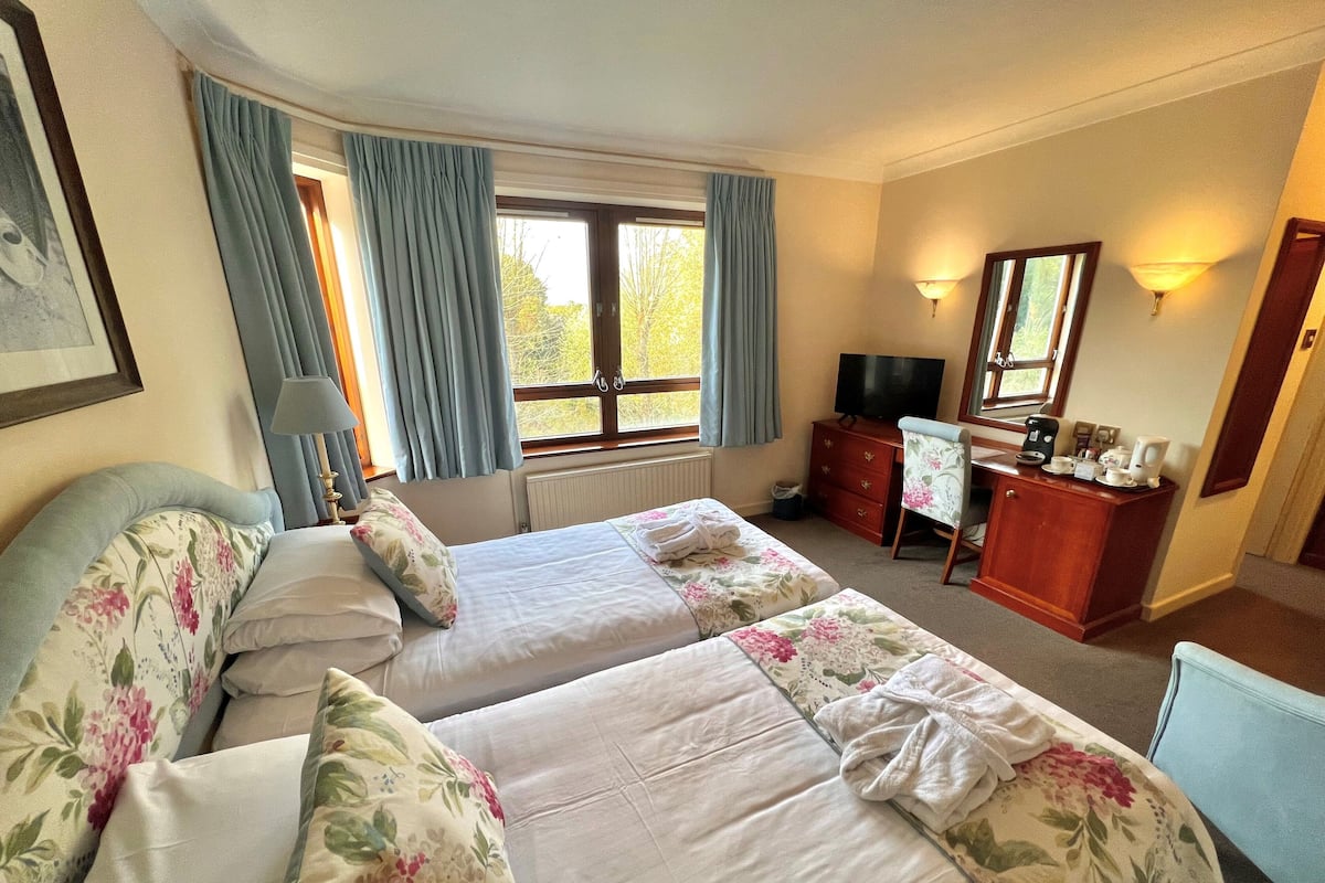 Une chambre d’hôtel avec deux lits, un bureau avec une chaise, une télévision et une fenêtre avec des rideaux.