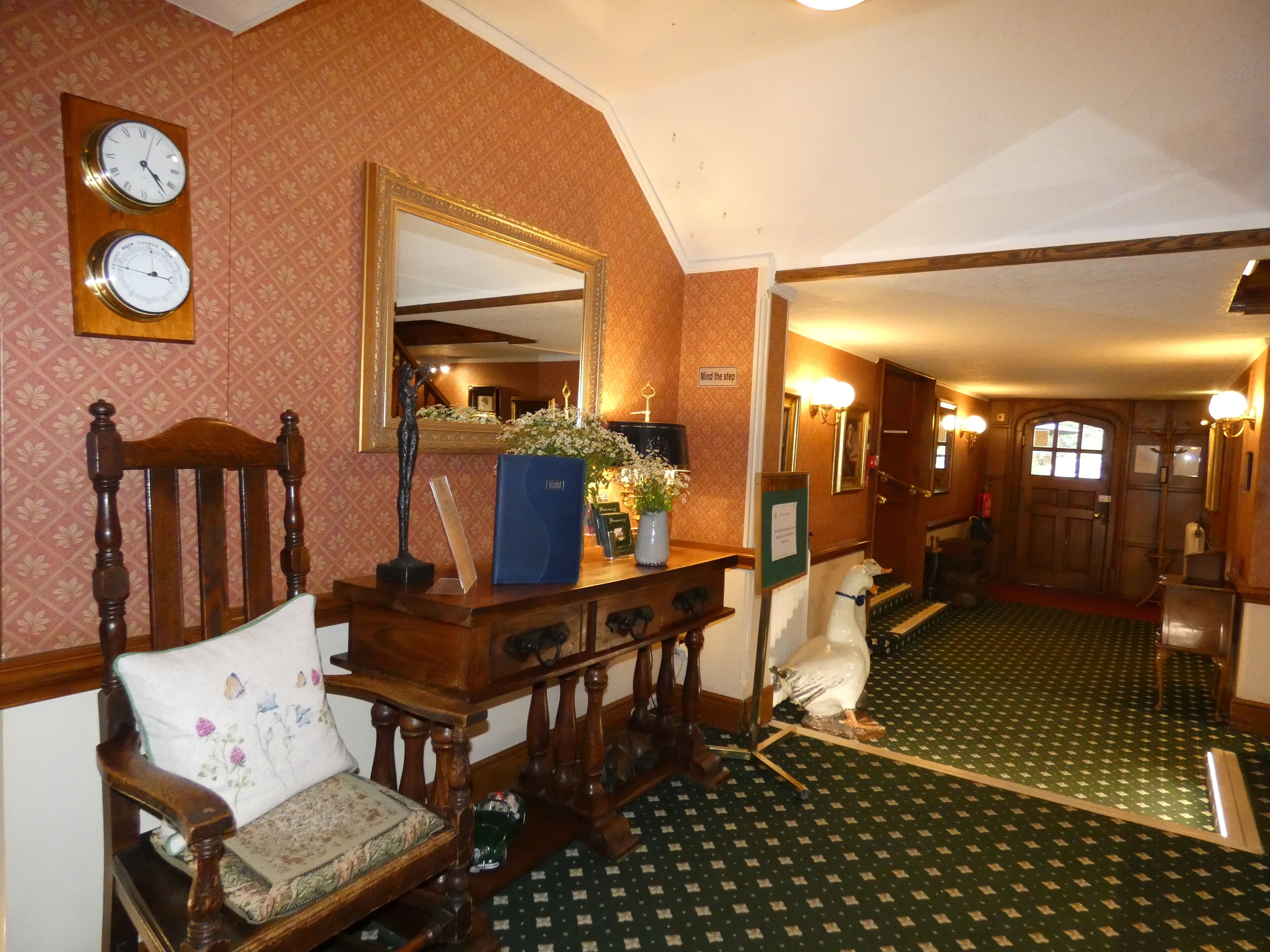 A traditional interior with a wooden chair, a mirror, clocks, and a green patterned carpet.