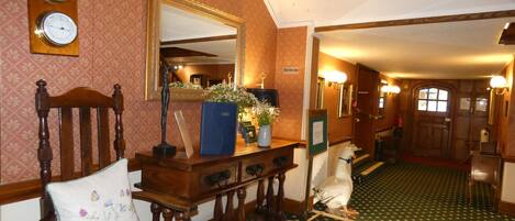 A traditional interior with a wooden chair, a mirror, clocks, and a green patterned carpet.