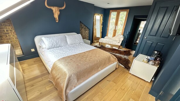 A bedroom with a bed, a white sofa, a wooden floor, a cowhide rug, a bull skull wall decoration, and a door with a window. - the crown loft (Kingston upon Thames)
