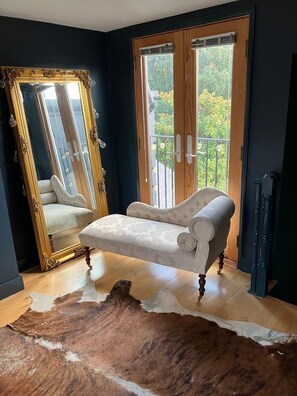 Una habitación con un espejo grande, un sofá, suelo de madera y vistas a través de una puerta.