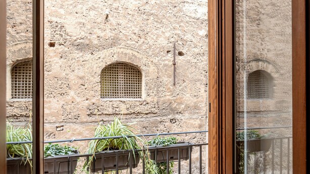 Une vue à travers la fenêtre d’un bâtiment aux murs de pierre et aux fenêtres en arc de cercle.