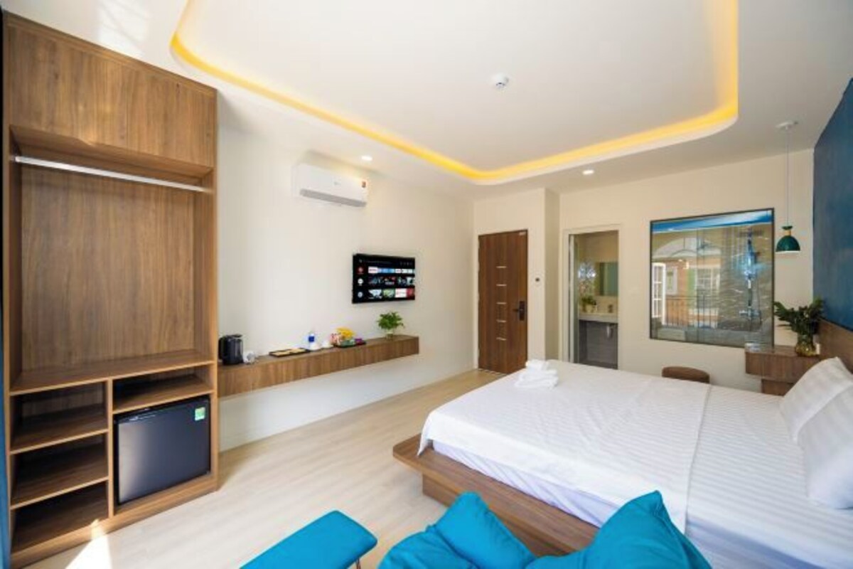 A modern hotel room with a large bed, built-in TV, and a wooden wardrobe.