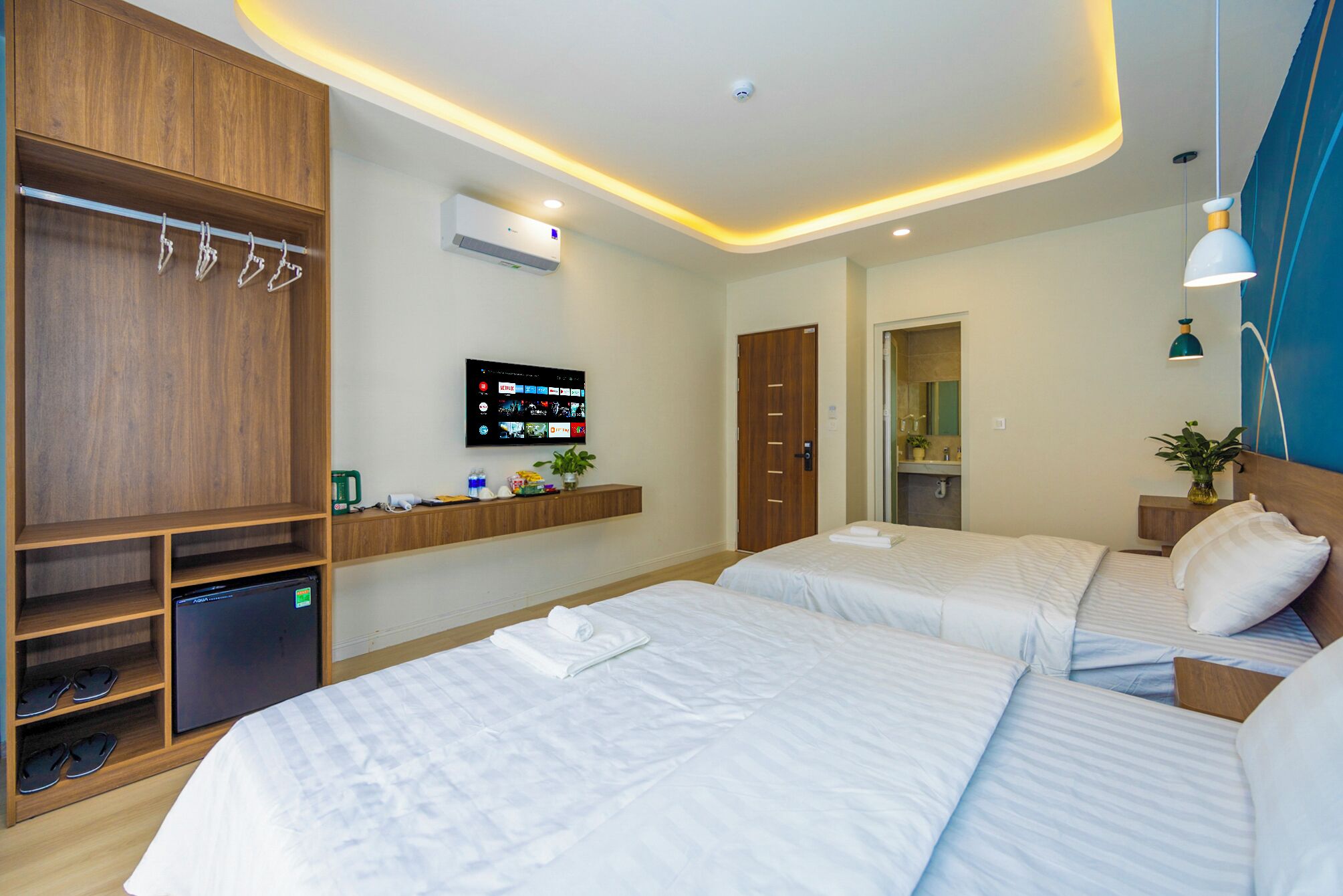 A hotel room with two beds, a TV mounted on the wall, a wardrobe, and a desk with a computer and a coffee machine.