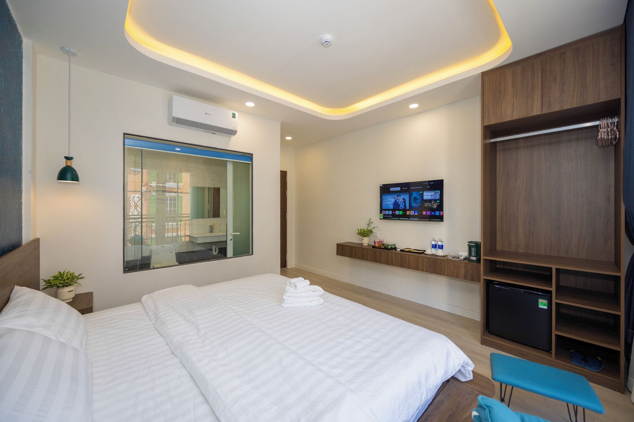 A modern hotel room with a large bed, a TV, a wardrobe, and a small seating area.
