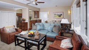 A living room with a sofa, two armchairs, a coffee table, and a dining area with a kitchen in the background.