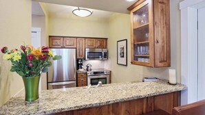 A kitchen with wooden cabinets, a granite countertop, stainless steel appliances, and a vase of flowers.