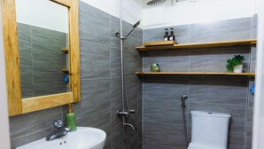 Een badkamer met een wit wastafel, een spiegel, een douche en een toilet. Daarboven, boven het toilet, bevinden zich houten planken.