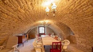 A stone-walled room with a wooden table and chairs, a chandelier, and a window with a view. - Le Clos du Prince, Country house with private pool and enclosed garden, ideal for families! (Saint-Vincent-Rive-d'Olt)