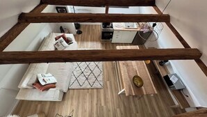 Un espai tipus loft amb bigues de fusta al descobert, una zona de cuina i un racó agradable per seure amb coixins i una catifes.