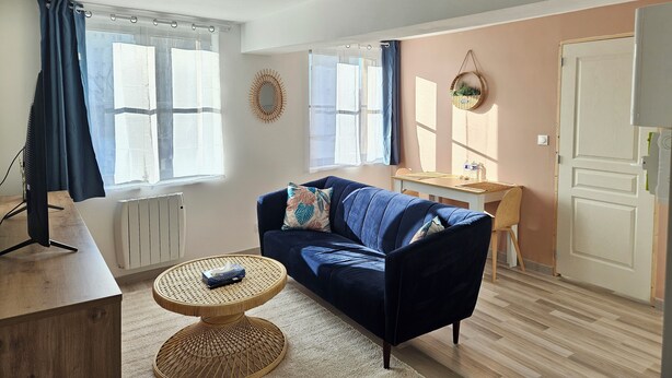 A living room with a blue sofa, a small round table, a TV, and a window with curtains. - Cosy apartments Valenciennes center Train station and streetcar on foot (Valenciennes)