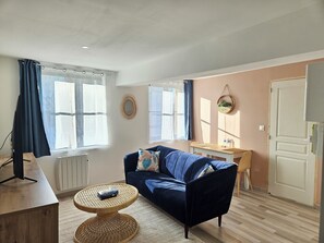 A living room with a blue sofa, a small round table, a TV, and a window with curtains.