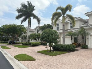 A residential area with a paved driveway, palm trees, and a white house with a tiled roof. - Luxury condo in the heart of Naples FL (Naples)