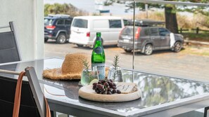 En balkon med et glasbord, der holder en flaske, en flettet kurv, en tallerken med druer og to glas med rosmarin.