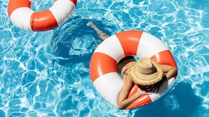 Una persona flotando en una piscina con un sombrero de paja, usando un flotador hinchable rojo y blanco.