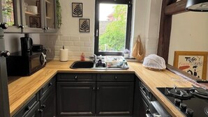 Une cuisine avec des meubles de couleur sombre, un plan de travail en bois, une cuisinière noire et une fenêtre donnant sur un paysage verdoyant.