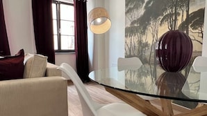 Un salon moderne avec une table à manger à plateau en verre, des chaises blanches, un canapé beige et un grand vase.