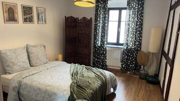 A bedroom with a bed, wooden wardrobe, and a window with patterned curtains.
