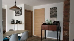 Un comedor con mesa de madera, sillas modernas, una lámpara colgante y un mueble bajo con botellas.