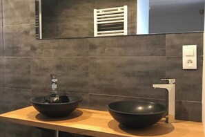 A modern bathroom with two black bowls on a wooden countertop, a white faucet, and a towel rack above a mirror. - Cozy Apartment (Sélestat)