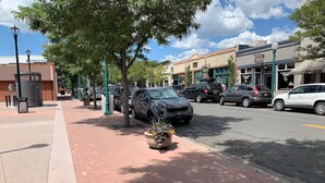 Une vue de rue avec des toilettes publiques, des voitures garées et des devantures de magasins.