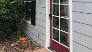 Une maison avec une porte rouge, des encadrements de fenêtres blancs et un petit porche.