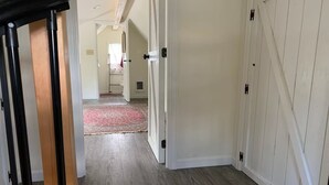 Un couloir doté d’un plancher en bois, de murs blancs et d’une porte donnant sur une autre pièce.