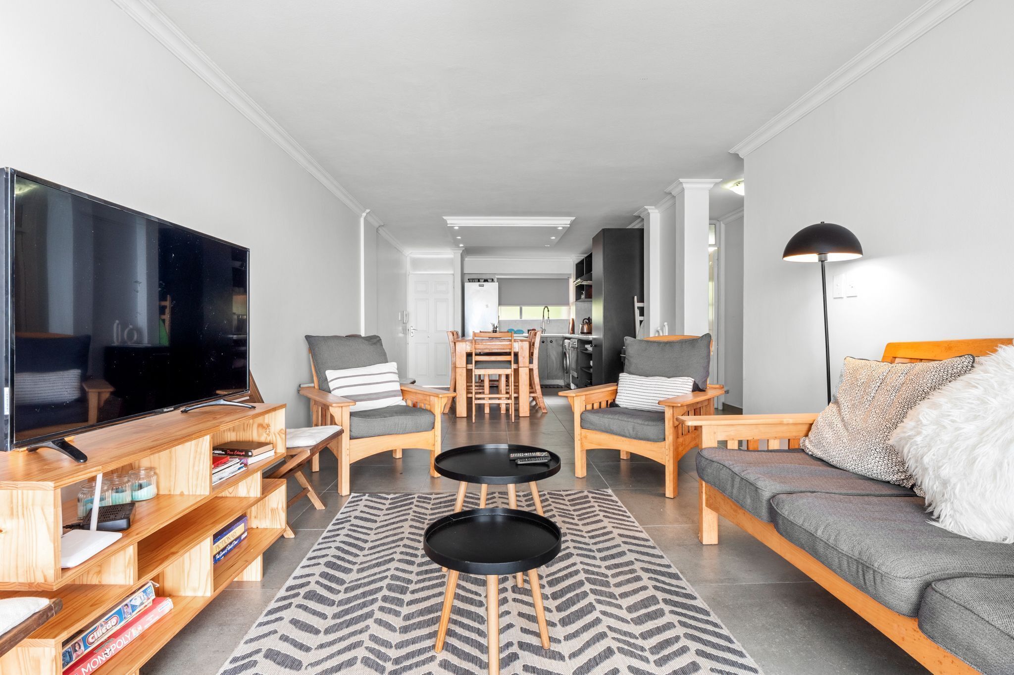 Un salon moderne doté d’un grand téléviseur à écran plat, de meubles en bois, d’un canapé et d’un coin repas à l’arrière-plan.