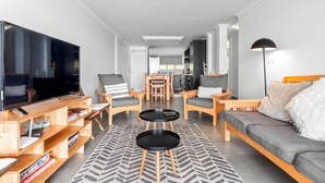 Una sala de estar moderna con un televisor de pantalla plana grande, muebles de madera, un sofá y un comedor al fondo.