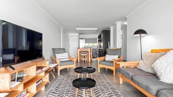 Un salon moderne doté d’un grand téléviseur à écran plat, de meubles en bois, d’un canapé et d’un coin repas à l’arrière-plan.