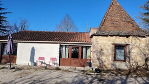 En bygning i sten med et tagtækket tag, en trädörr og et lille vindue. To klapstole og et bord står udenfor.