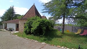En lille steng bygning med et kegleformet tag, omgivet af grøn vegetation og en grusbelagt indkørsel.