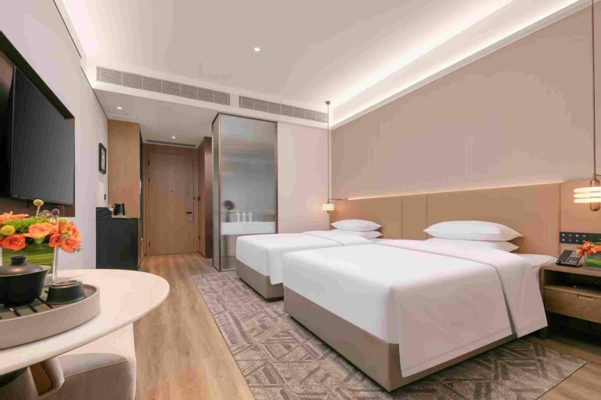 A hotel room with two beds, a dining area, a TV, and a bathroom.