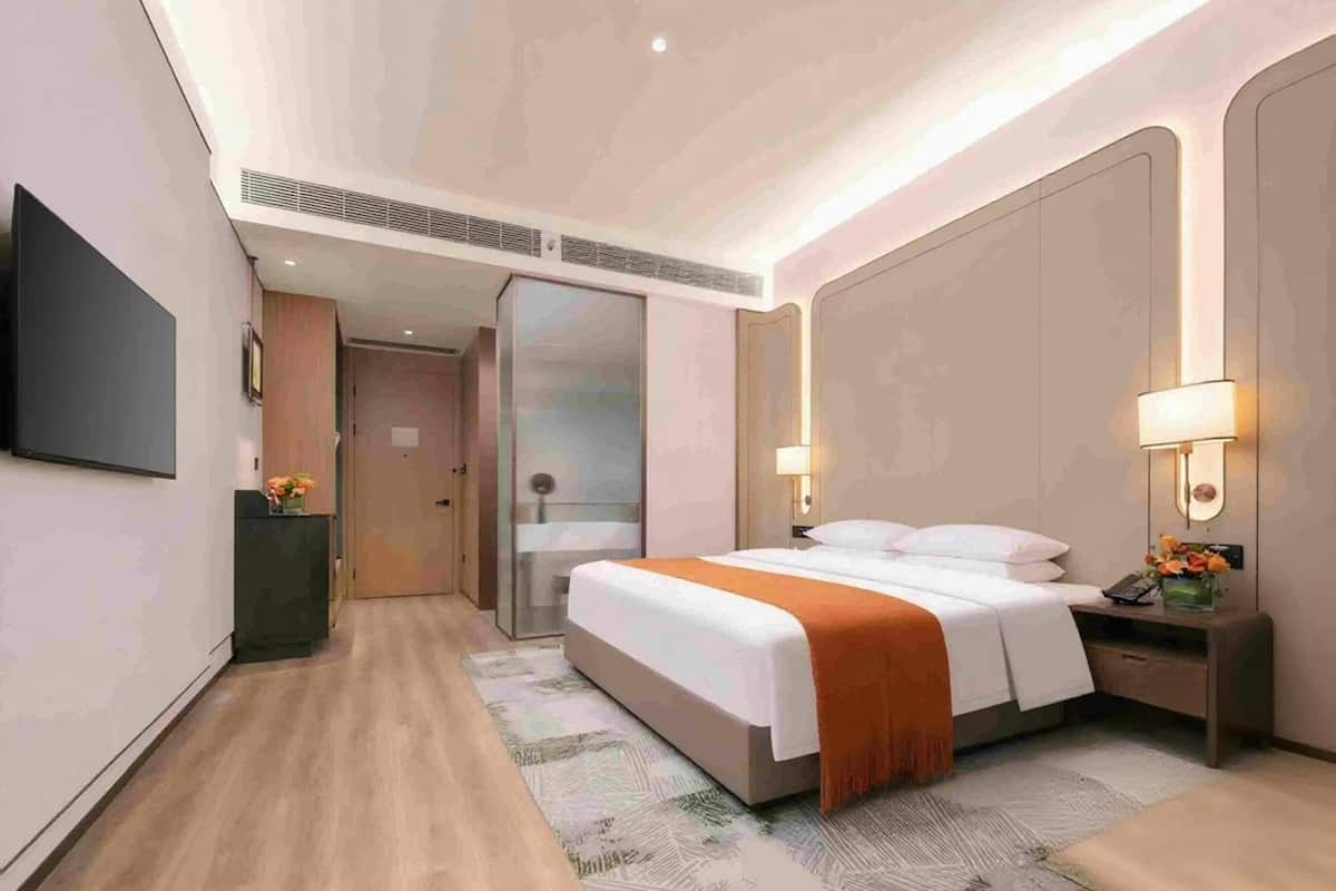 A hotel room with a bed, bedside table, lamp, and a TV mounted on the wall.