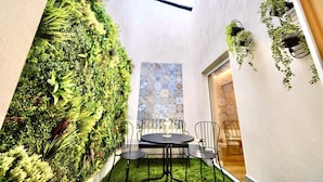 A narrow indoor space with a vertical garden, a round table with chairs, and a patterned wall.