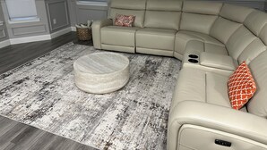 Ein modernes Wohnzimmer mit einer Eckcouch, einem runden Couchtisch und einem gemusterten Teppich.
