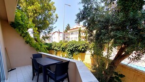 A balcony with a table and chairs, a mop leaning against the wall, and a view of buildings and trees. - Mar Soleil Apartments (Marmaris)