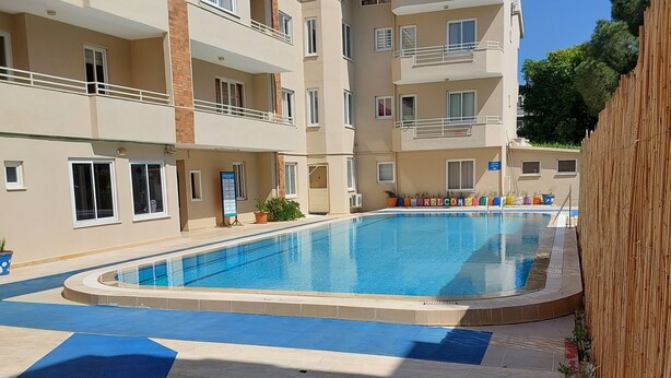 A swimming pool surrounded by a multi-story building with balconies and a wooden fence. - Mar Soleil Apartments (Marmaris)