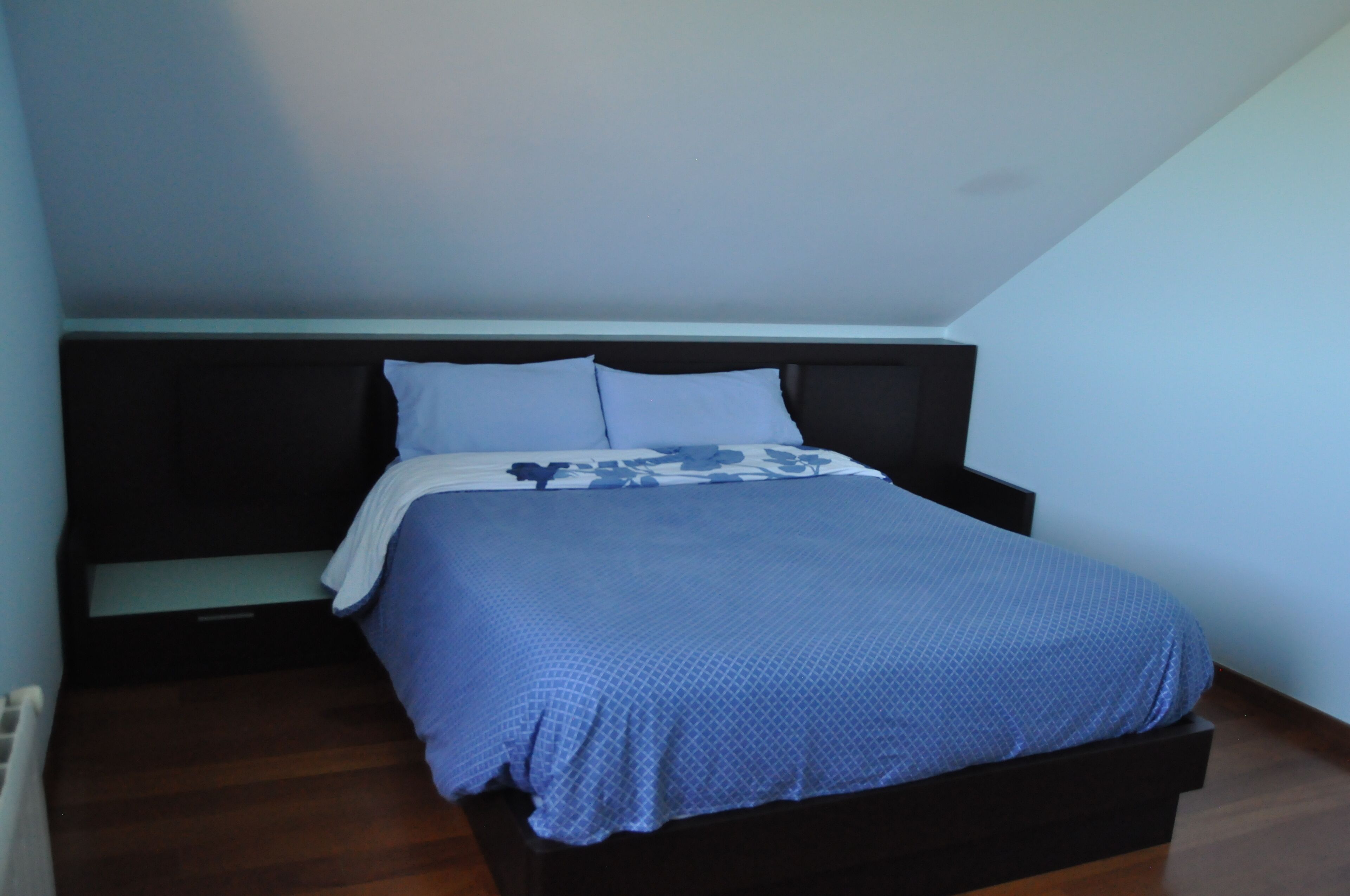 Un dormitorio con cama, cabecera y mesita de noche.