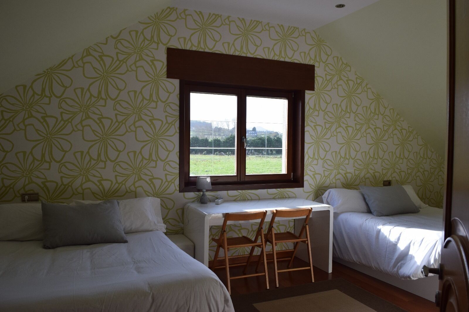 Une chambre avec deux lits, un bureau et une fenêtre donnant sur un champ verdoyant.