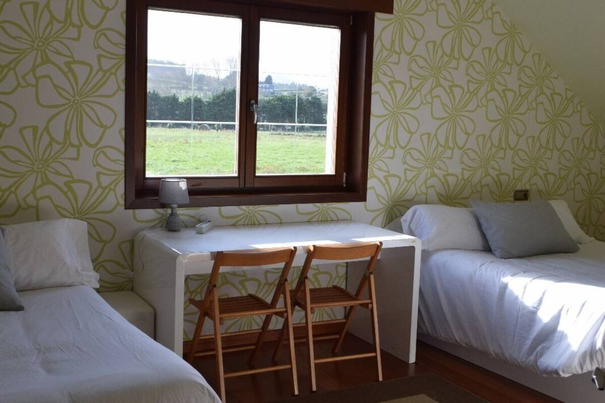 A bedroom with two beds, a desk, and a window.