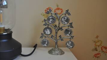 Un arbre décoratif en métal, orné de cadres photo circulaires sur ses branches, est placé sur une table devant un mur recouvert d’un papier peint à motifs floraux.