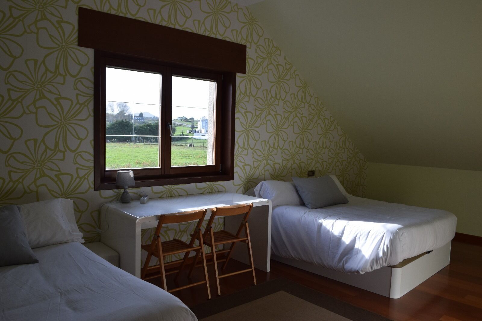 A small, single-room accommodation with two single beds, a desk, and a chair.