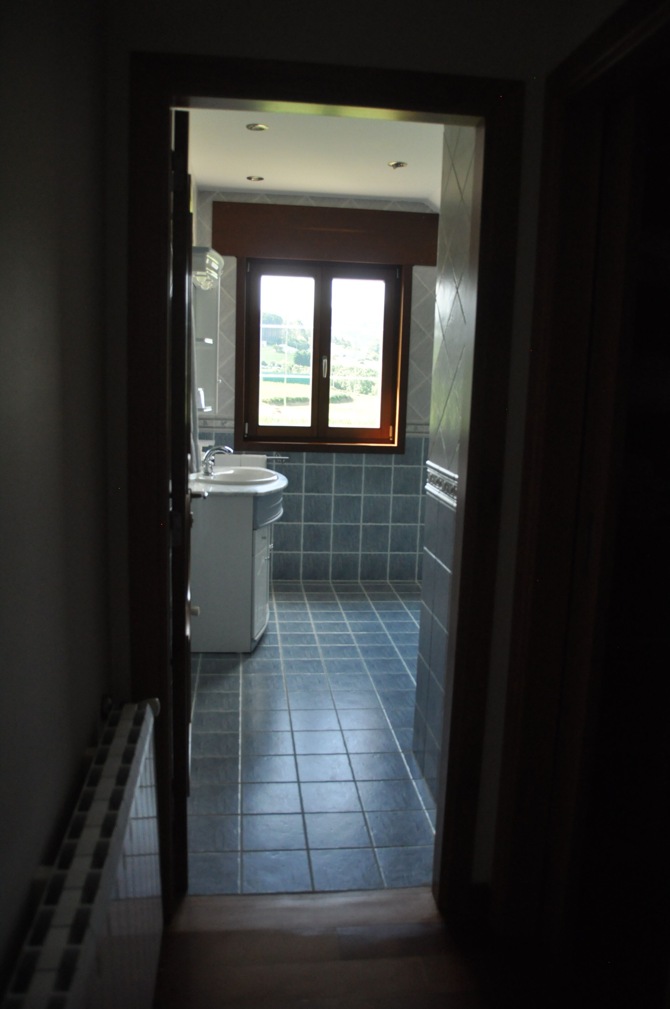 Un pasillo estrecho que conduce a un baño con ventana, lavabo e inodoro.