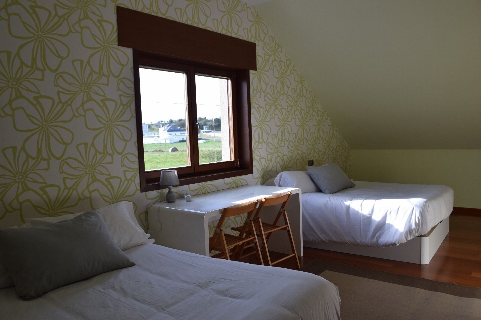 Una habitación con dos camas, un escritorio y una ventana con vistas a un campo.